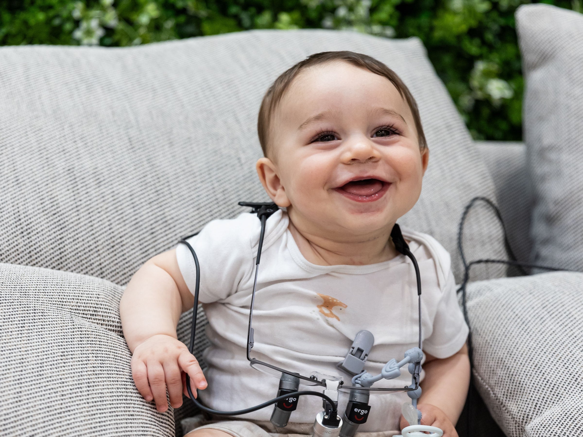 A baby laughs on the sofa in the clinic's lounge, dental loupes around their neck
