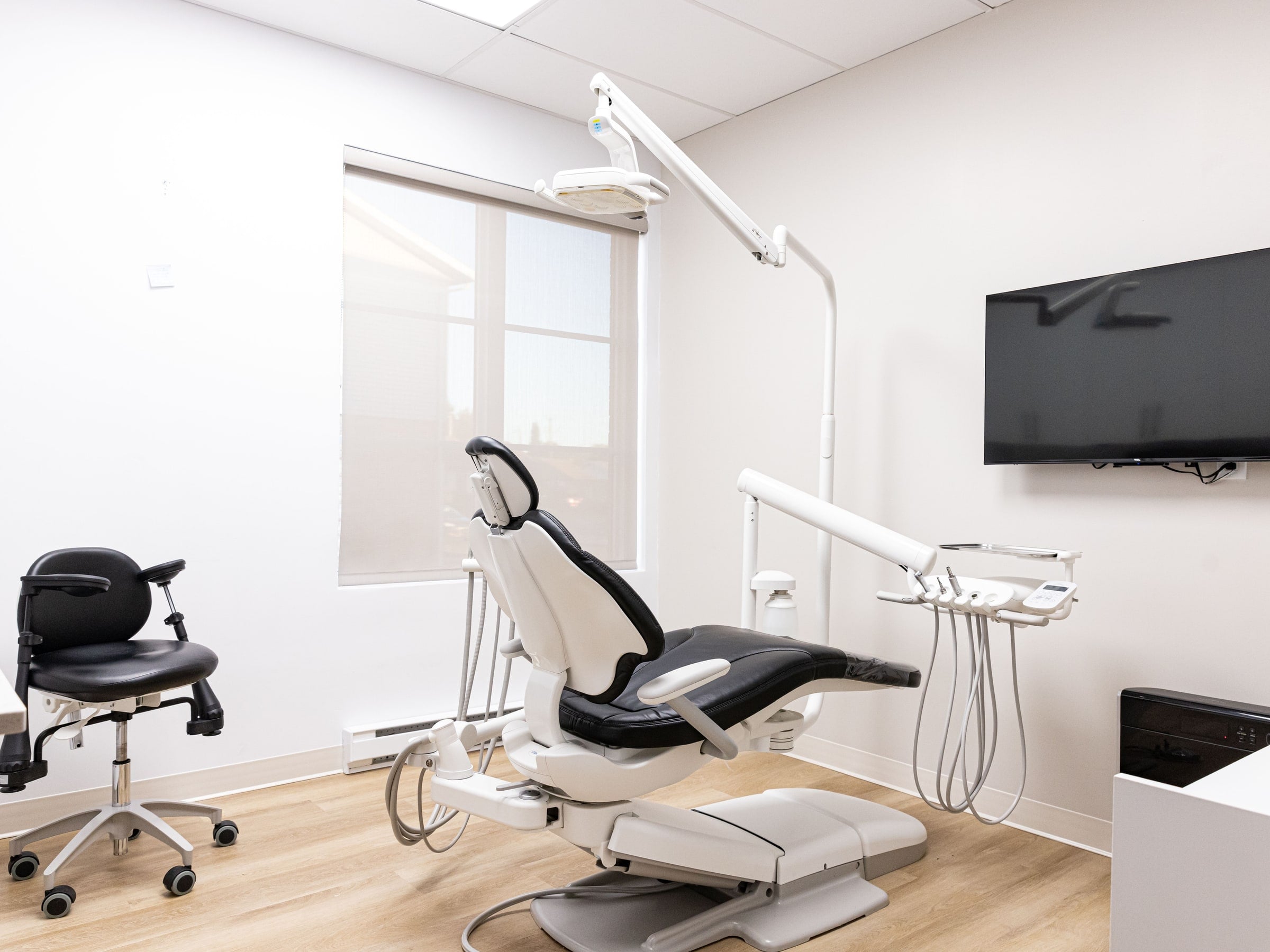 Une salle de traitement lumineuse : fauteuil, unité de soins, écran et grande fenêtre