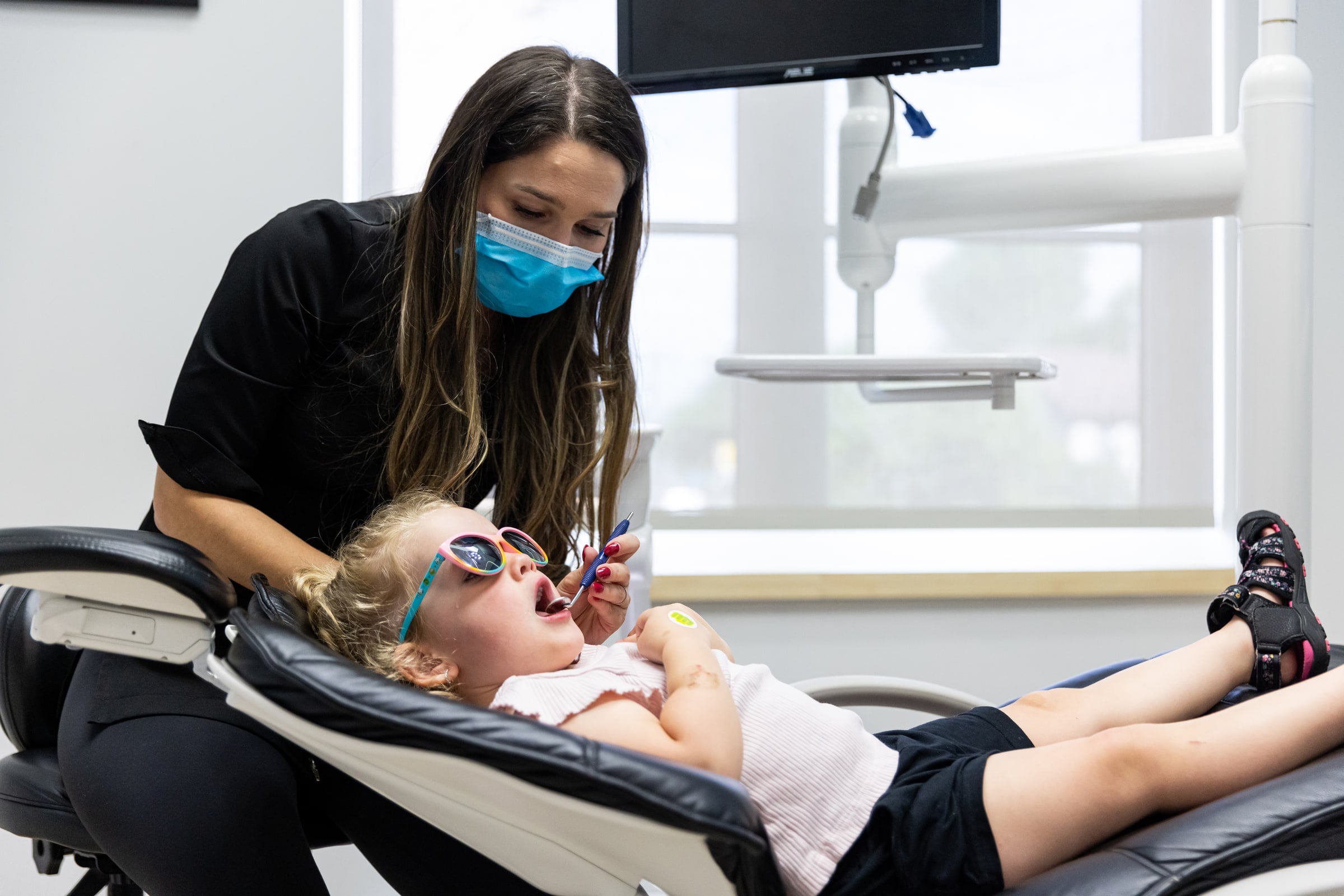 One of our dentists examines a young girl wearing sunglasses